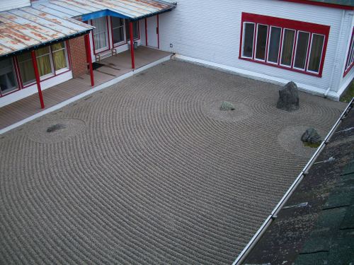 The author completed this raking pattern (the result of about 5-hours work with help from several curious meditators) in early October 2016, specifically as an offering to the practitioners sitting in the adjacent (behind the 6 red-framed windows) practice space known as the "Main Shrine Room." Of all the patterns produced thus far, this is the simplest and yet resonates the most energy from what I have known as "The Buddha Rock" or the largest rock protruding from the earth closest to the Main Shrine Room. Encircling the large stone created a pattern of ripples that fills the entire garden space. Simpler, quieter, one-ring ripples encircle the 4 stones that represent islands (like the "Buddha Rock") amidst the wave-action of the teaching Buddha (and all Buddhist teachers), to form the precious three jewels of the Buddha, the dharma, and the sangha--all represented here by way of a single stone and concentric circles. Before The Year of the Fire Monkey ends, and before the calendar year of 2016 ends, the author plans to offer one more raking in the coming weeks prior to the first week of November. Because of the passing of the author's mother, and because of the changes ahead, the next pattern could be very different. The author's practice of karesansui here at what Chögyam Trungpa Rinpoche, in 1970, named, "The Tail of the Tiger" has given him a mind-body synchronization practice--within a sacred space--that has resulted in a strong appreciation for an ancient and traditional Japanese, Zen-monastic practice. The author plans to remain involved in the upkeep, uplift, and future of this particular example of a small, temple-style dry landscape garden. P.S. Though it appears simple, the challenge of completing the final encirclings (four stones, one of which cannot be seen in this lovely photograph, with photo-credit thanks to Mr. G. Vu) was difficult....namely entering and exiting the two "disciple" stones, or Buddha's children--the two stone/islands flanking the Buddha stone to the right and left--and finally, touching up and exiting at the Buddha stone. The final operation of raking the single "frame" line was straightforward, and--as the author has told others (and through consultation with our resident Feng Shui expert), improves the feng shui of the garden. My this garden help others contemplate impermanence, joy, and the six perfections as they manifest in the phenomenal and psychological worlds of the contemplator. Thanks to the Vidyadhara for creating this garden; thanks to everyone who has supported and acknowledged the author's practice in this subtle space; and thanks to the stones. May (as the Natives say when sometimes referring to stones...) the " wise ones" continue to offer a space of phenomenal quietude and yet, contemplative insight, and may the garden itself thrive and benefit all sentient beings, especially those who visit this space/place and feel the dralas that have been felt and carefully embraced by the karesansui raker. With hopes of continuing to practice the contemplative art within this space in the coming years, thanks to Mr. A. deLong for giving me the first opportunity to explore what has become a most profound and energizing meditative and contemplative practice. Chi-me Chönying 